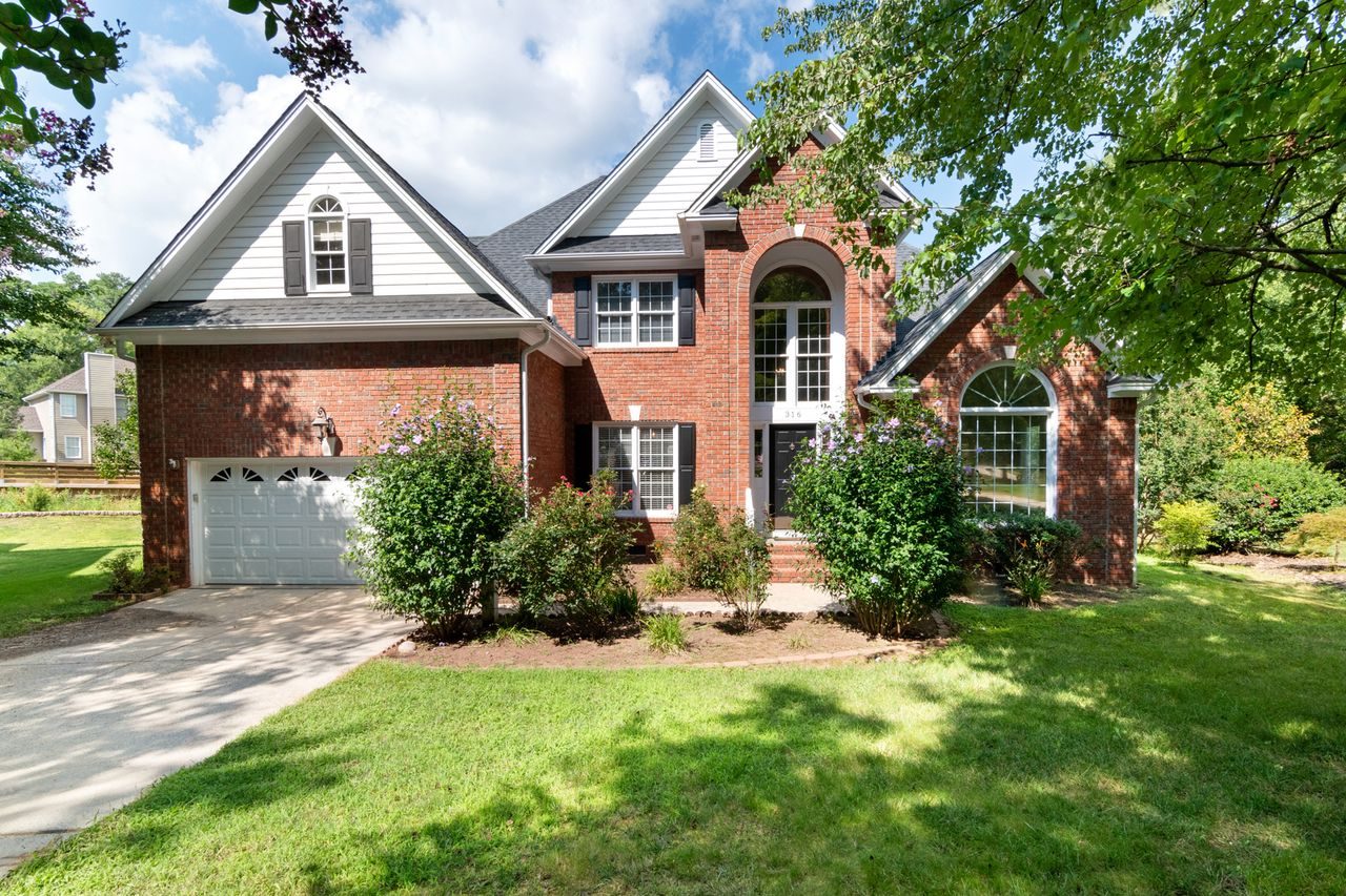 A two-story brick house with a front lawn and a two-car garage on a suburban street