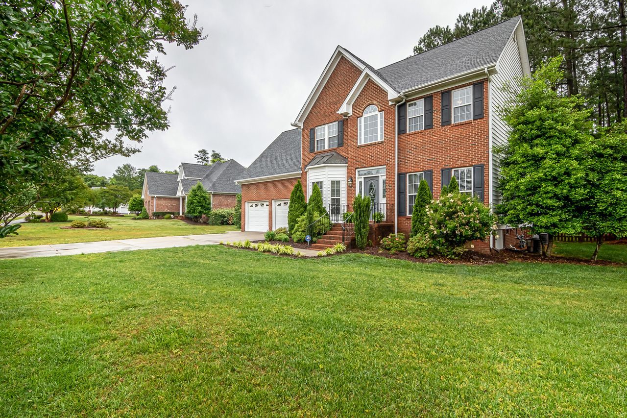 A brick two-story house with a wide lawn in a suburban neighborhood