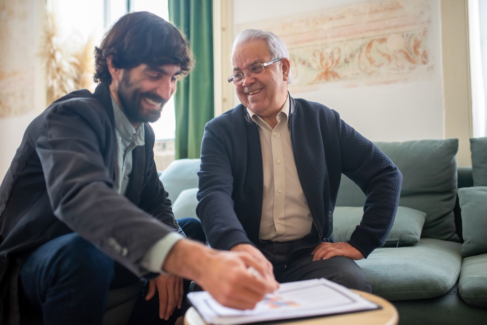 A younger man and an older homeowner smiling while reviewing a document together
